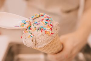 An ice cream in a waffle cone getting sprinkles added to it by spoon.