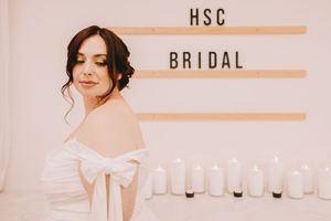 A woman in a bridal gown looks over her shoulder. It says HSC BRIDAL behind her with a counter full of candles.