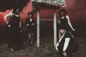 a group of women in witches hats are posed around an old well with red smoke filling in behind them.