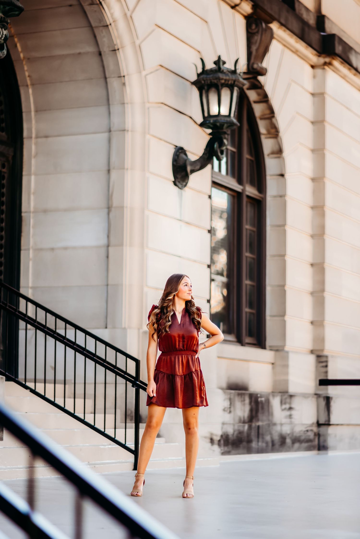 Woman in red dress posing elegantly on marble steps near classical architecture.