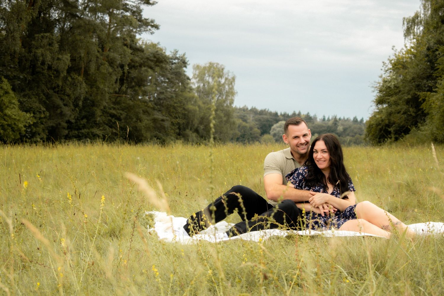A couple relaxes together on a blanket in a sunny meadow.