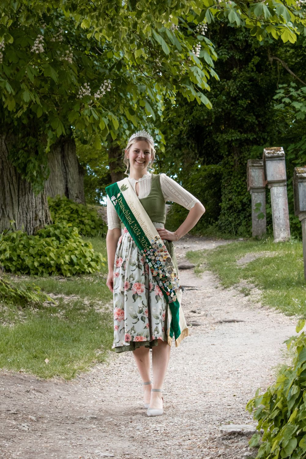 A series of four images showing someone wearing a floral dress and green scarf walking along a tree-lined gravel path.