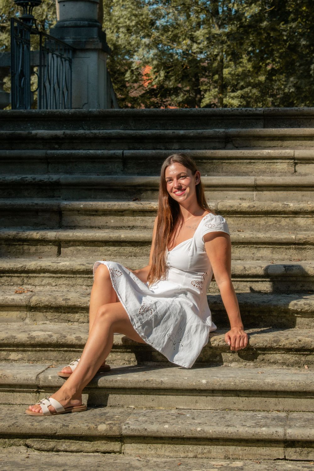 A white dress figure reclines on stone steps in a natural outdoor setting during a sunny day.