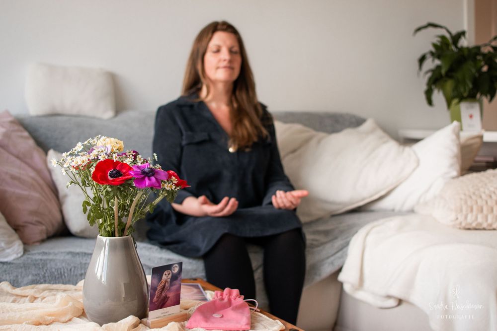 Someone relaxing on a gray couch with decorative pillows and fresh flowers in a vase on a nearby table.