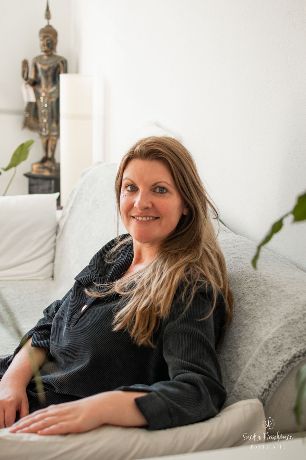A person in a black sweater relaxes comfortably on a white couch with decorative statues visible in the background.