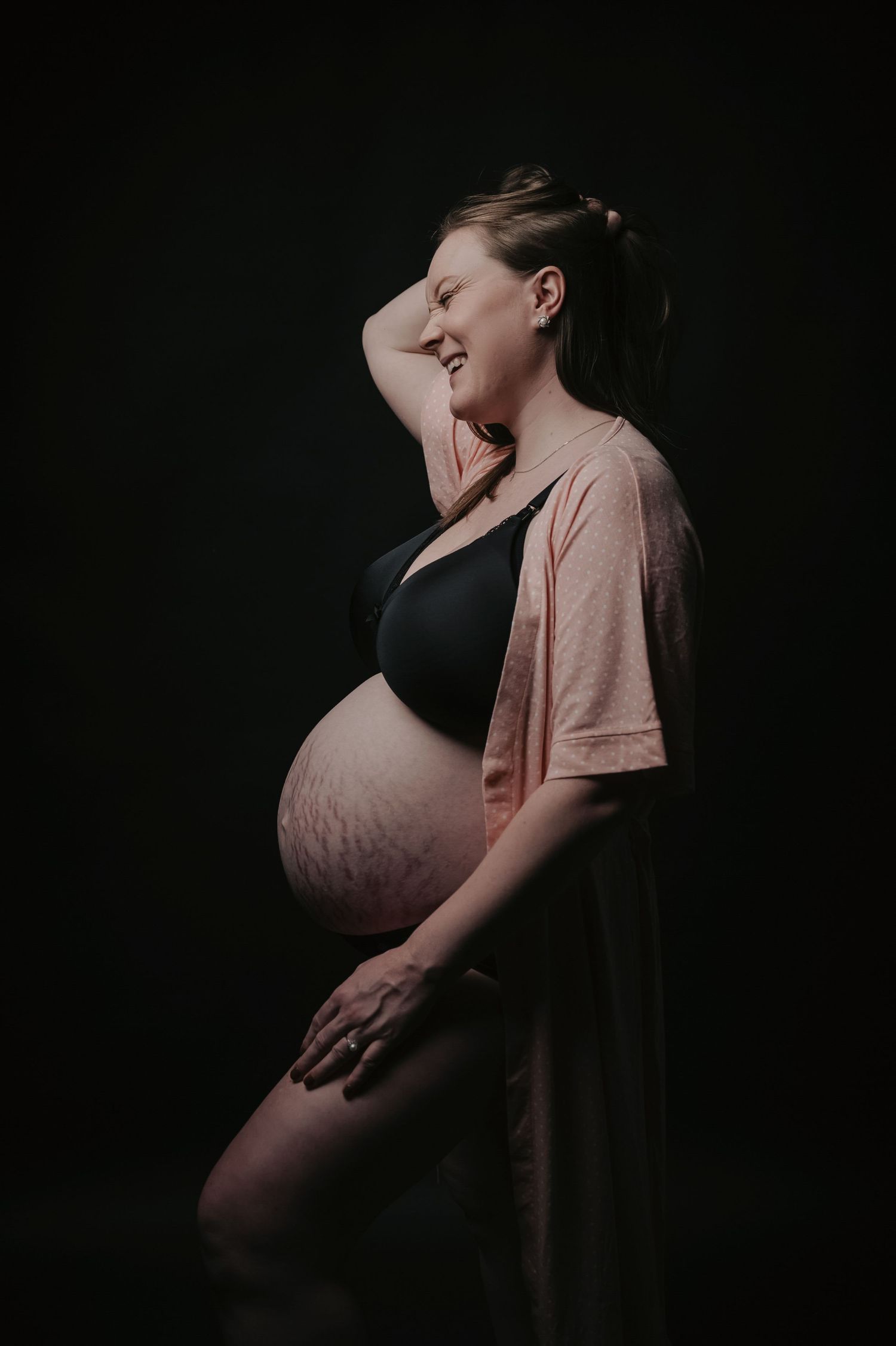 Dramatic silhouette maternity portrait against dark background.