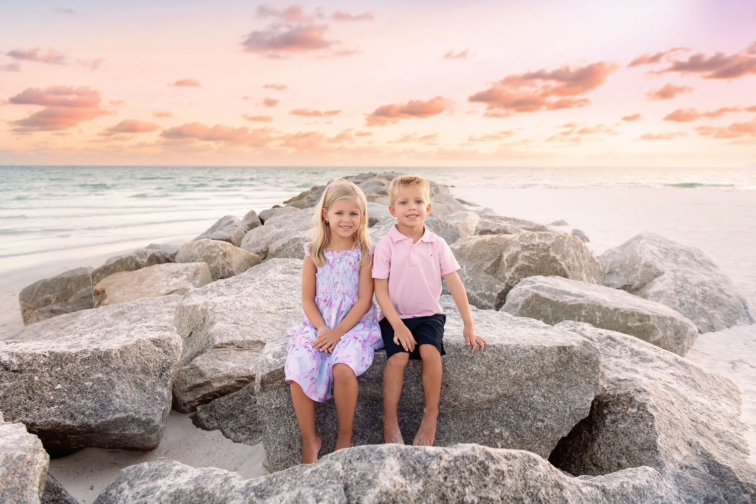 Coastal family photography session on rocky beach during golden hour sunset.
