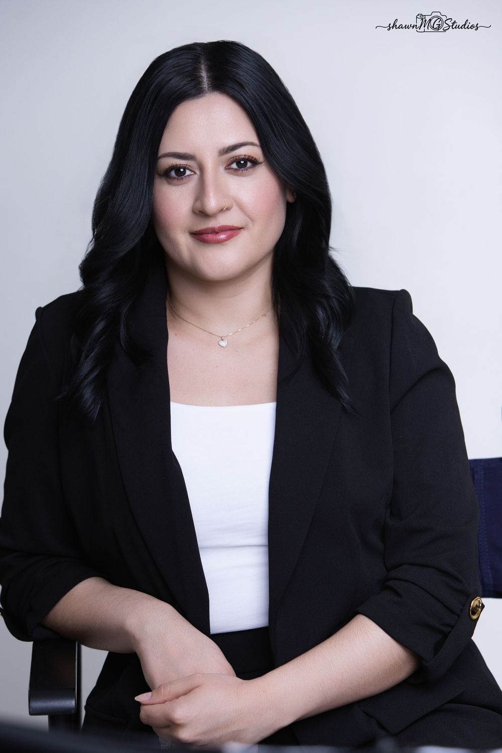 Professional woman in black blazer and white top poses confidently for a corporate headshot photo.