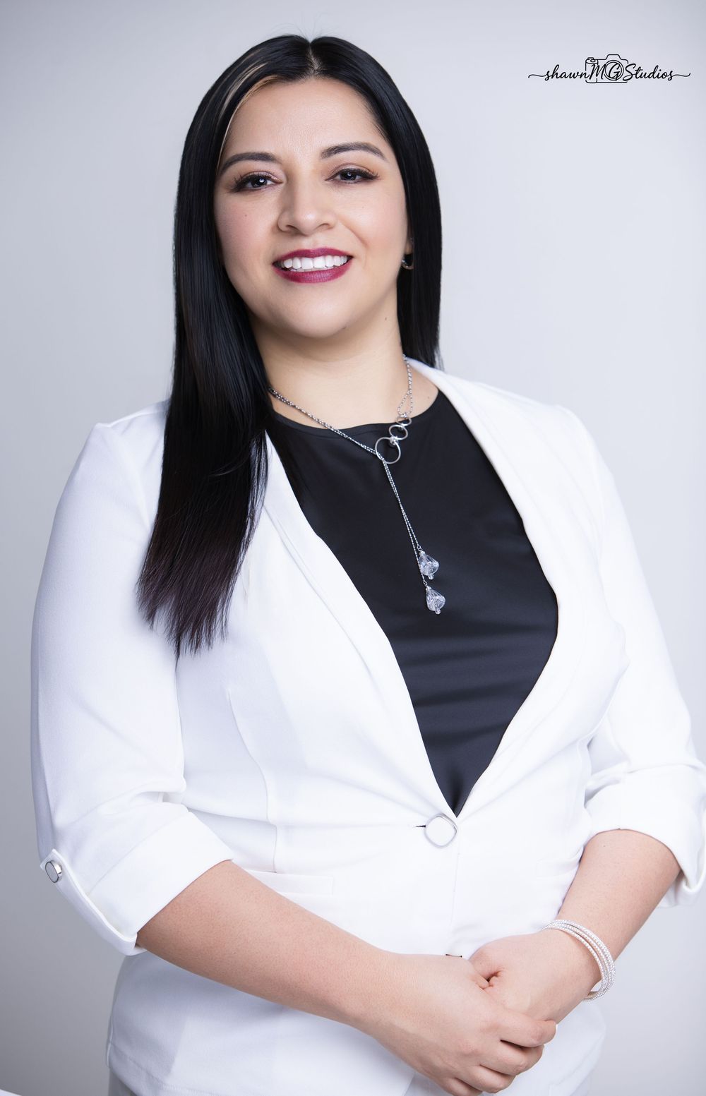 Professional woman in white blazer and black top smiling confidently for a corporate headshot photo.