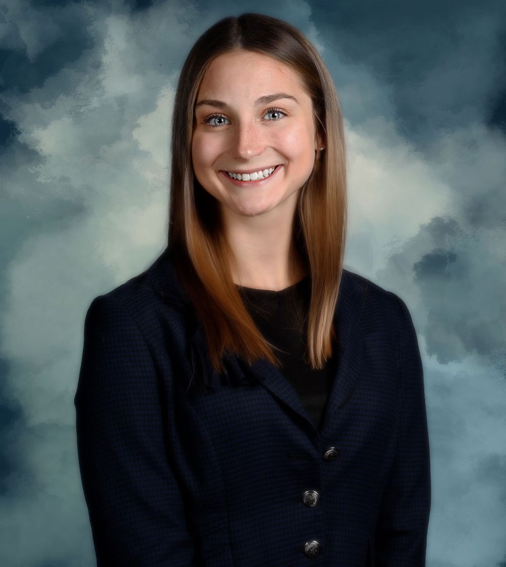 Professional headshot against a dramatic cloudy background in formal black attire.