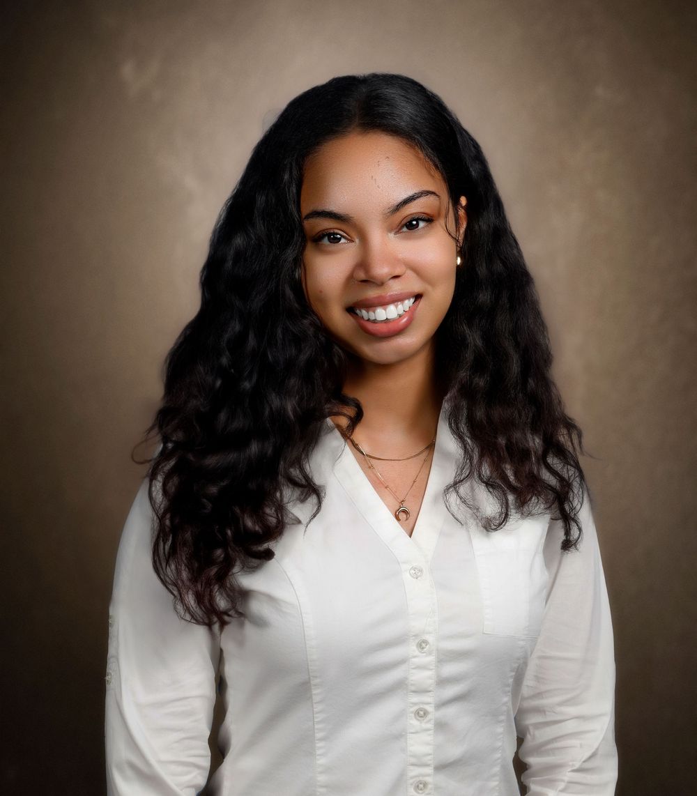 Professional studio portrait in white button-down shirt against brown backdrop.