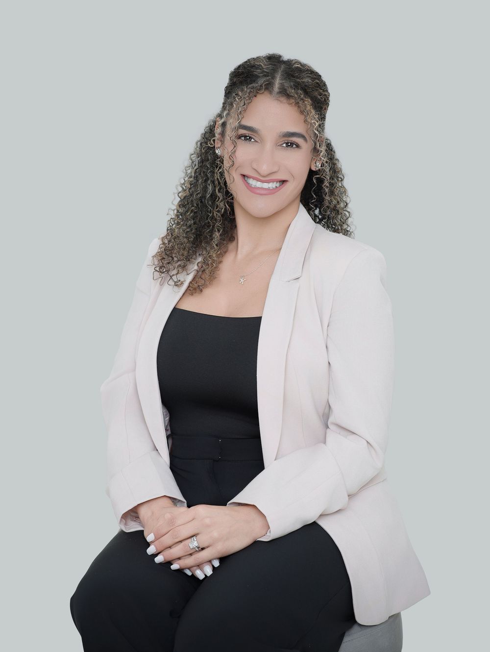 Professional headshot against gray background wearing light pink blazer and black top with curly hair.