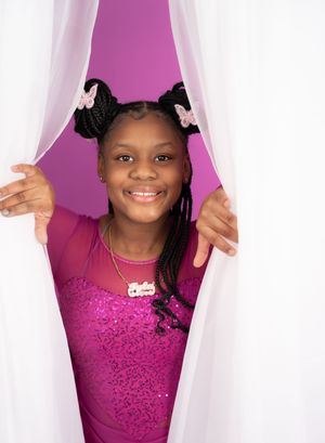 Performer in sparkly purple leotard peeks through white curtains with a bright smile.