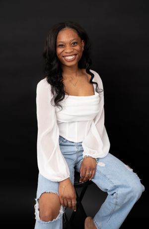 Casual studio portrait in white top and blue jeans against dark background.