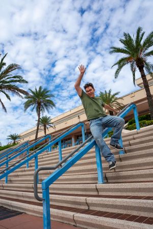 Person posing on concrete steps with palm trees and blue sky in background.