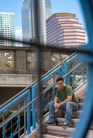 Person sits along urban railing with modern city buildings in background during daytime.