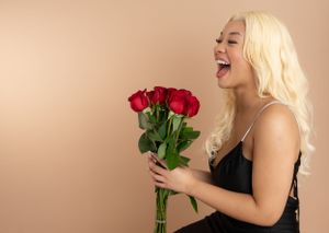 Elegant portrait series holding red roses in a black dress against warm beige background.