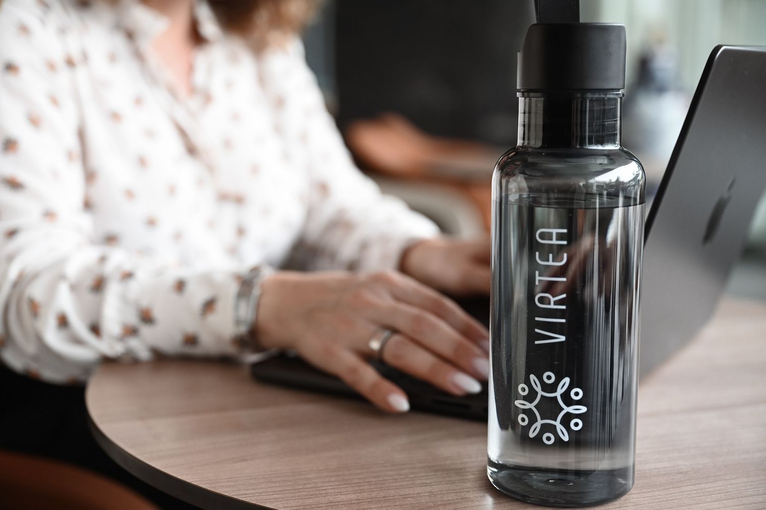 Person typing on laptop with reusable black water bottle labeled Match on wooden desk.