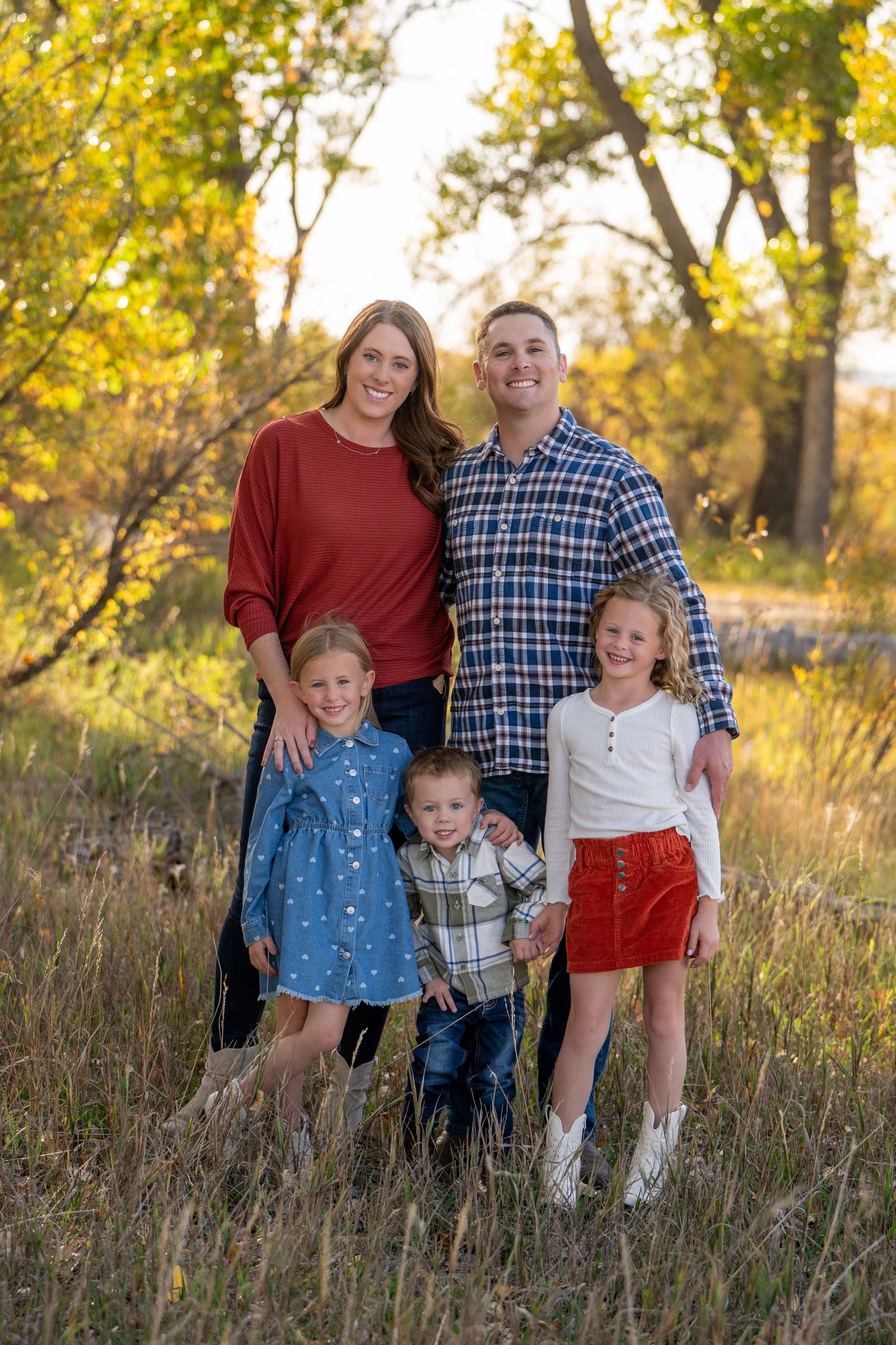 Family group portrait in fall scenery with golden lighting and tall grass.