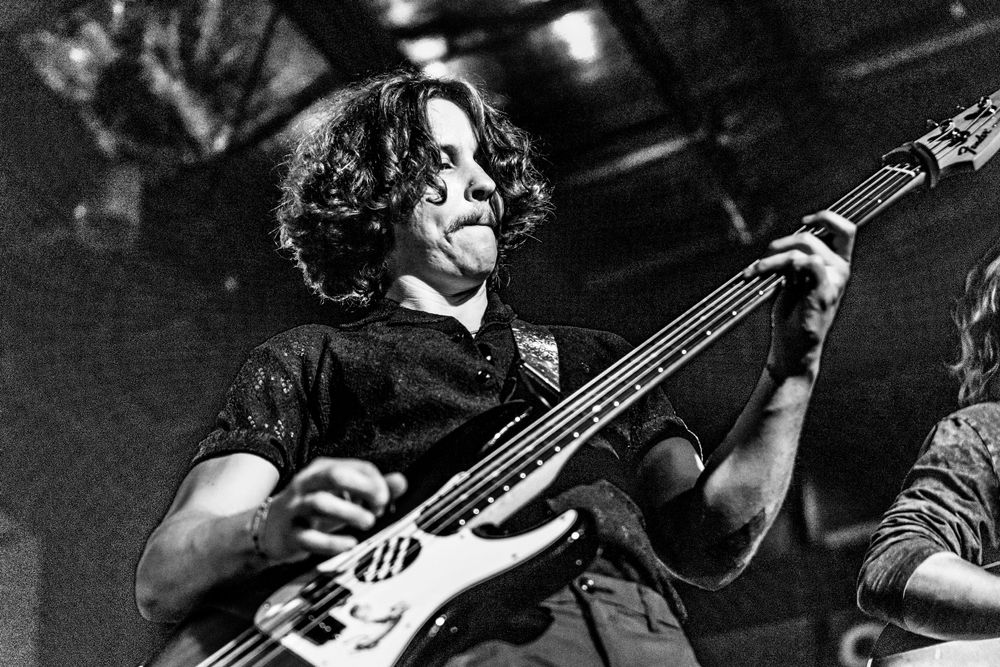 Musician performs passionately on electric bass guitar during a dark concert setting.
