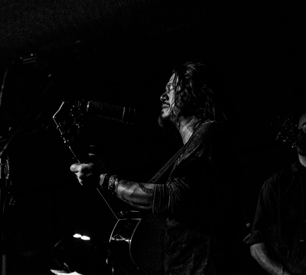 Dramatic black and white photo of musician playing guitar on dimly lit stage.