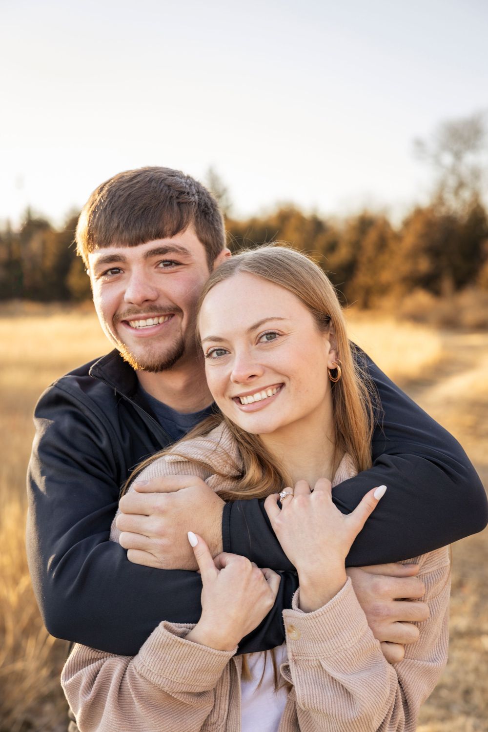 Couple embraces in a golden field during sunset for an engagement photo.