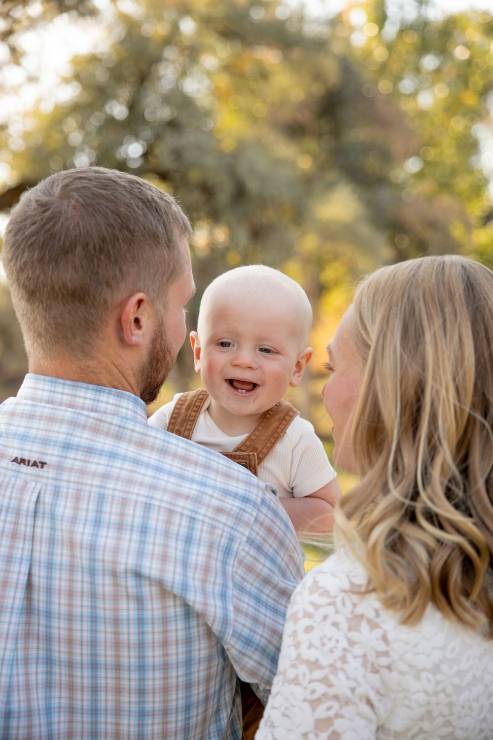 Happy baby laughing while being held by parents outdoors during autumn.