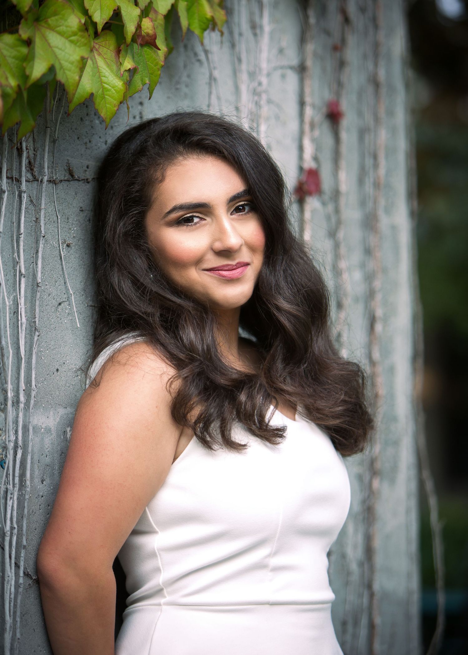 A smiling teenaged girl is leaning with her back on a concrete wall