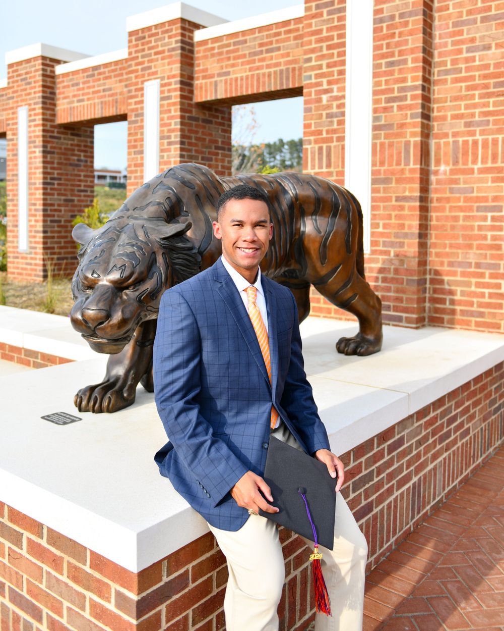 Person in blue suit poses with large black panther statue on brick pedestal.