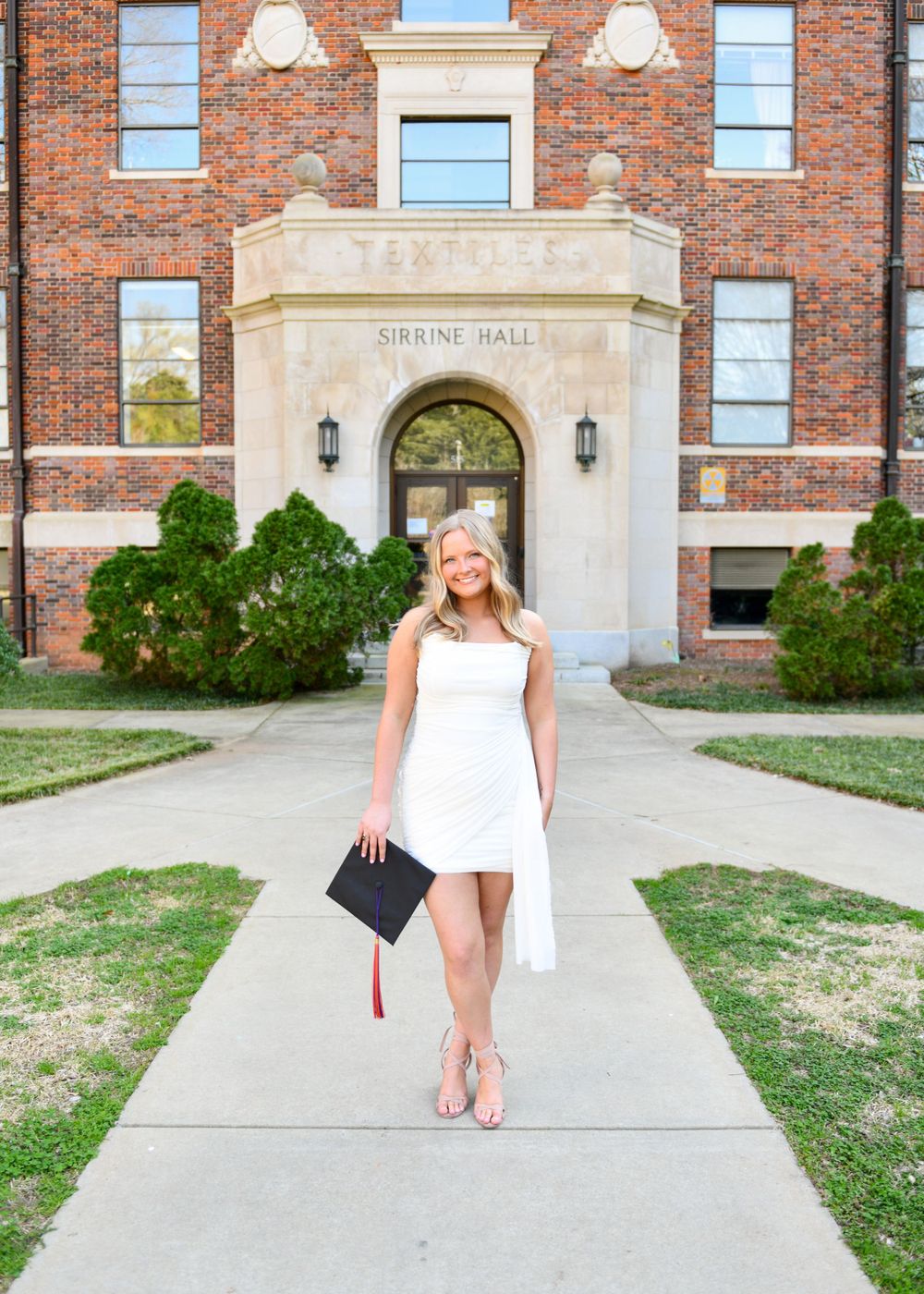 Graduate in white dress poses in front of brick Science Hall building entrance.