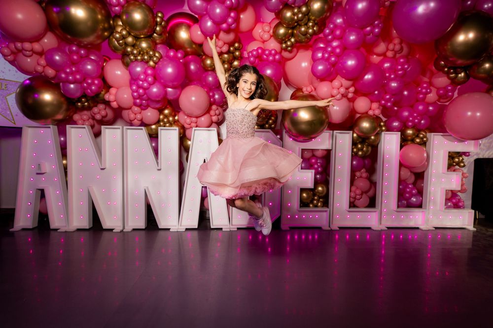 Bat Mitzvah girl jumps in front of a pink balloon wall - Bat Mitzvah Photography