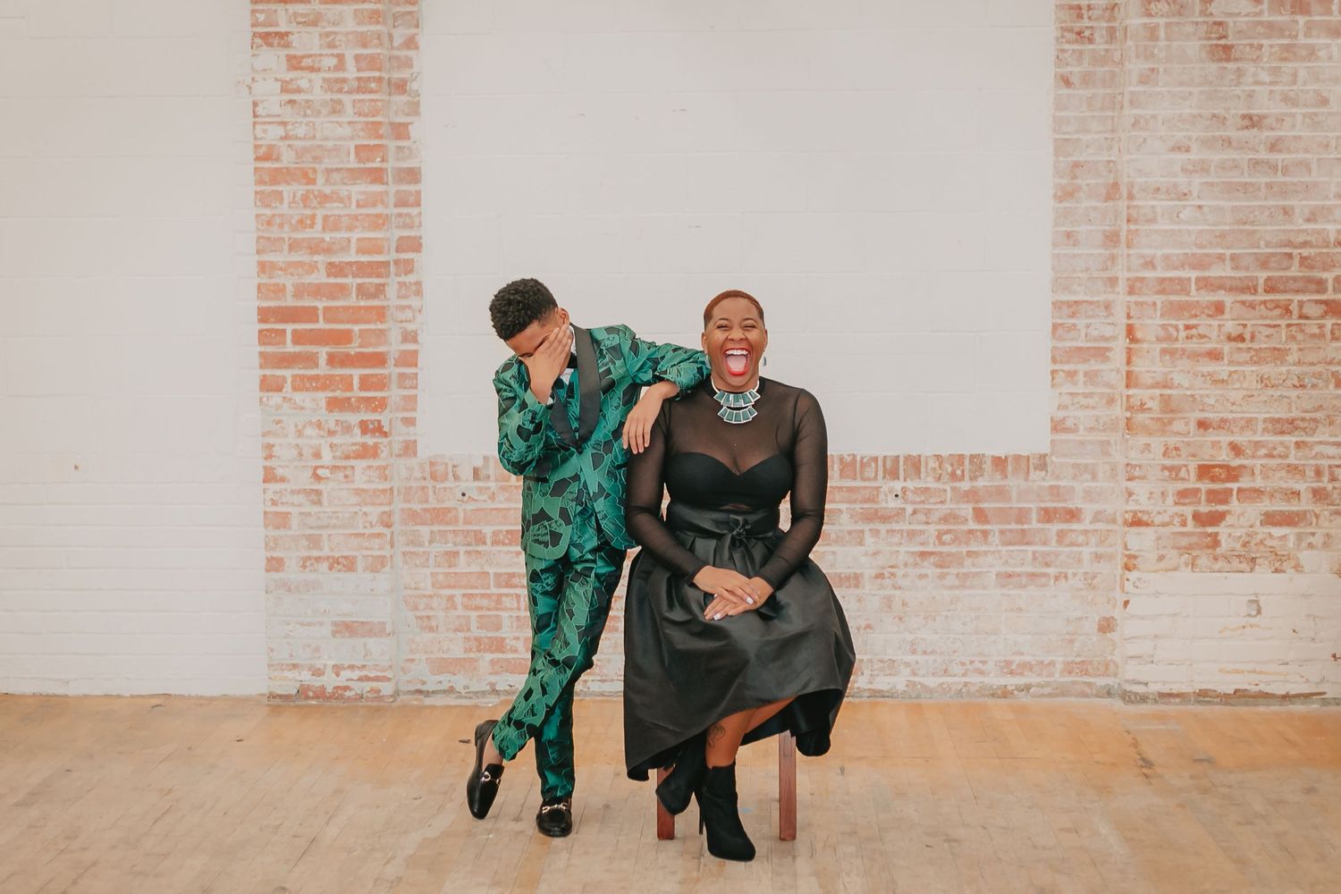Playful wedding party members pose and dance in an industrial brick-walled venue.
