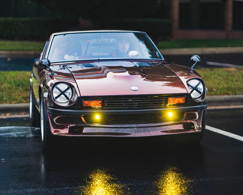 A classic brown sports car with pop-up headlights photographed at dusk.
