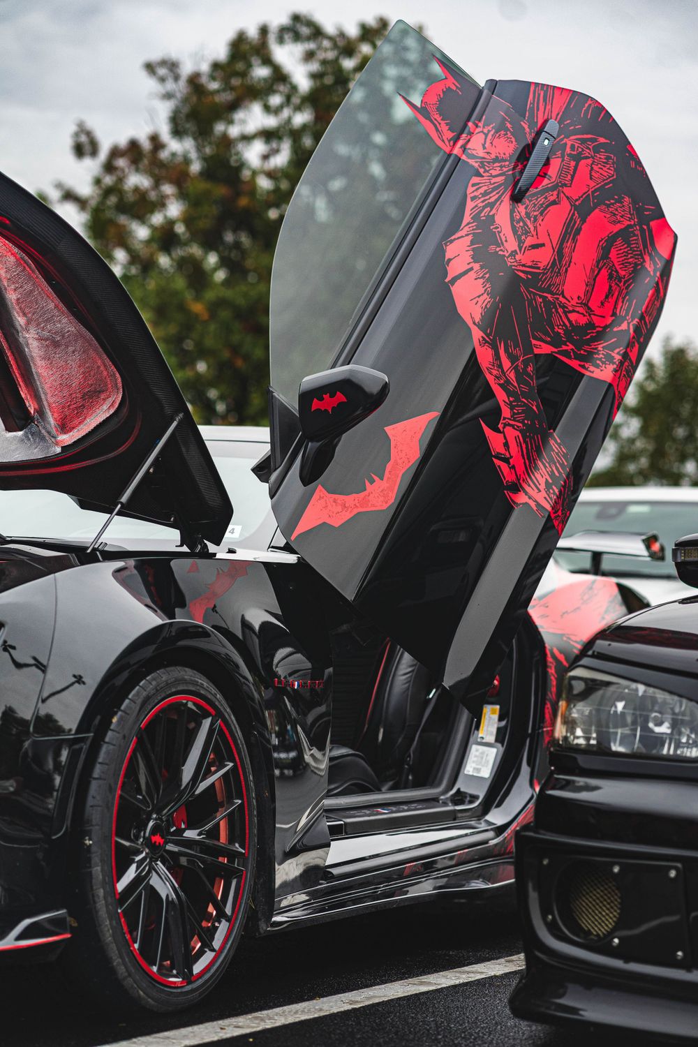 Custom black sports car with red accents and dramatic scissor doors displayed at a car show.