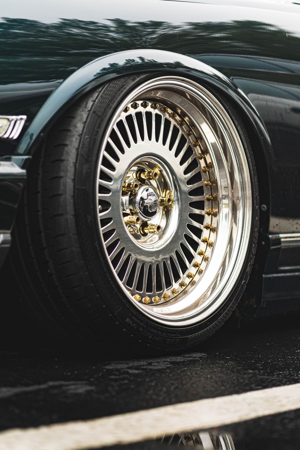 Chrome multi-spoke wheel rim with gold center cap mounted on black vehicle.