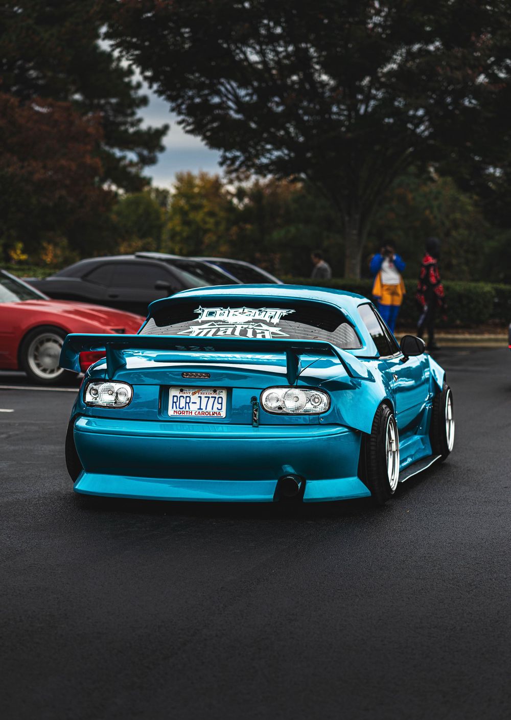Modified turquoise Mazda Miata with custom body kit and lowered suspension parked at dusk.