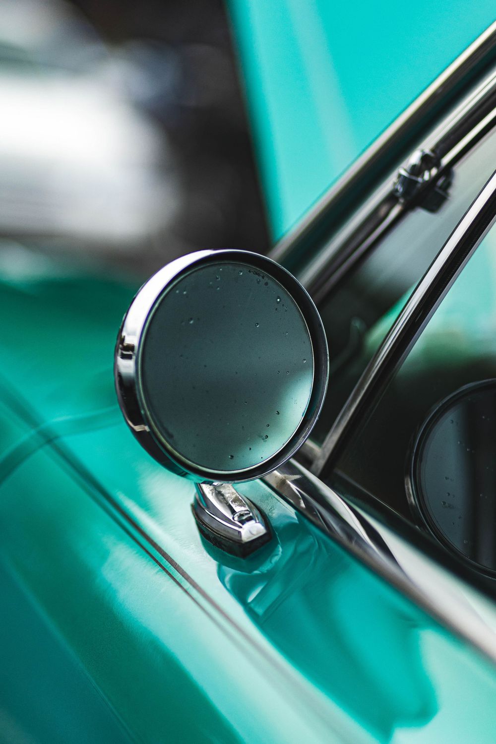 Close-up of a vintage chrome side mirror on a turquoise car.