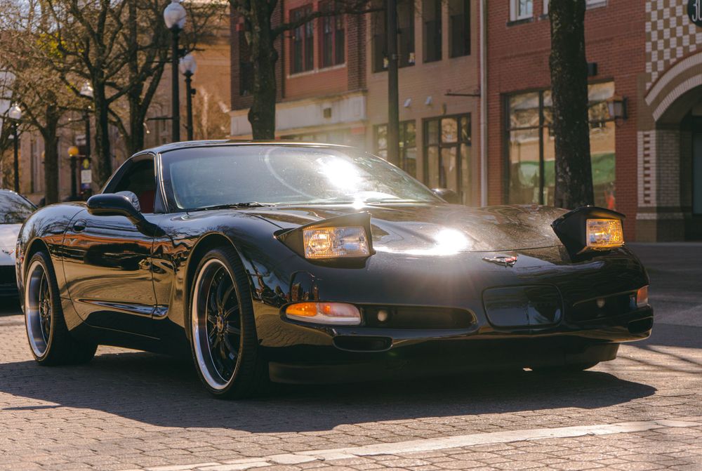 Black C5 Corvette with custom wheels parked on brick pavement.