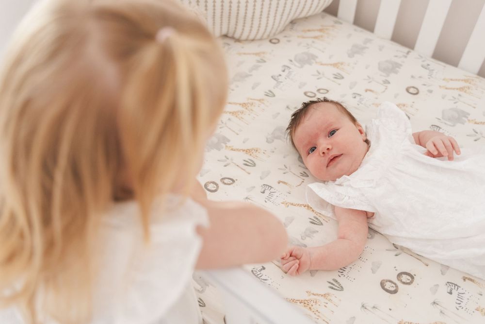 A tender moment between a toddler and baby sibling lying in a white crib.