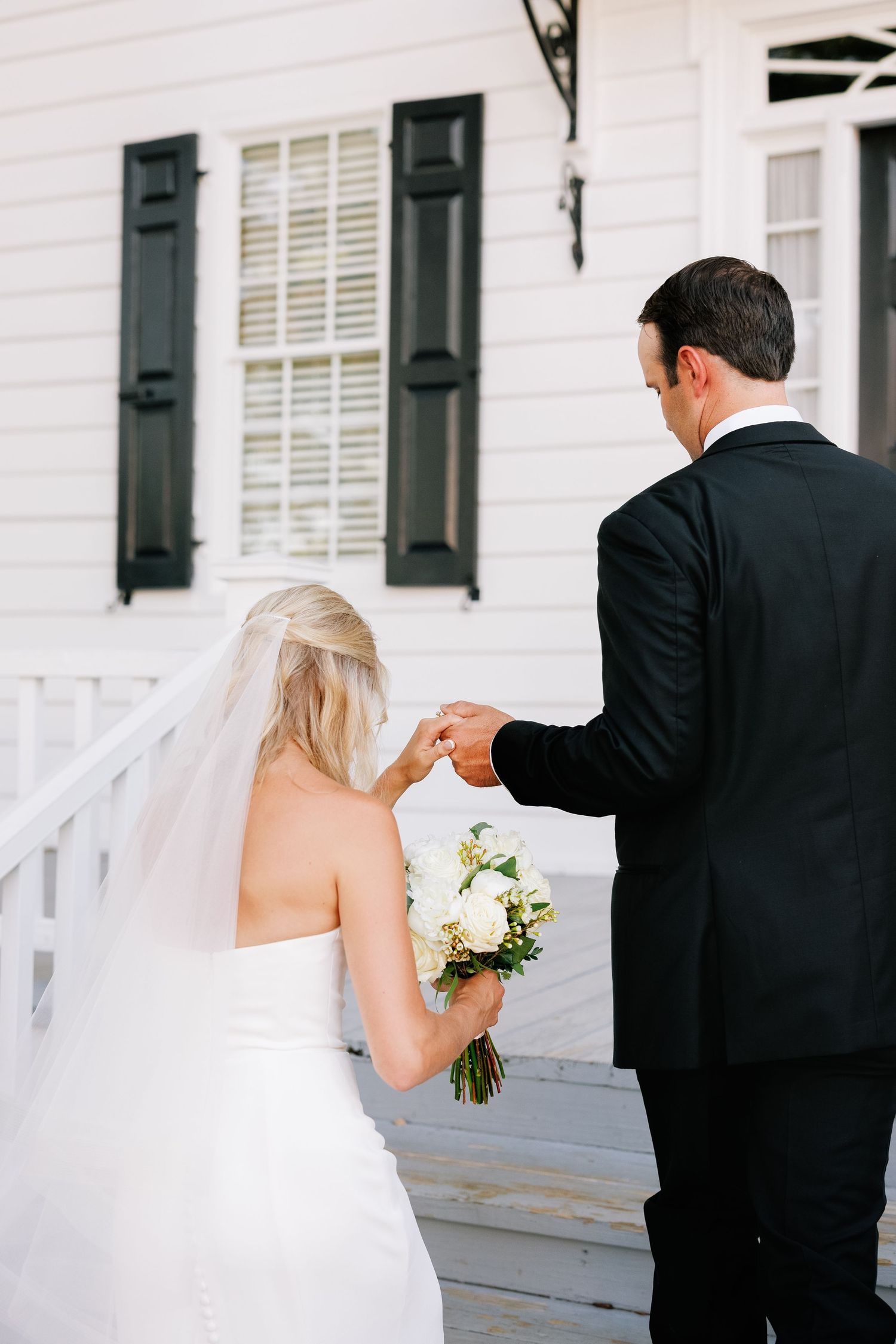 A groom lending her hand to an elegant bride to assist her while walking up stairs at the Kaminski House, in Georgetown, SC