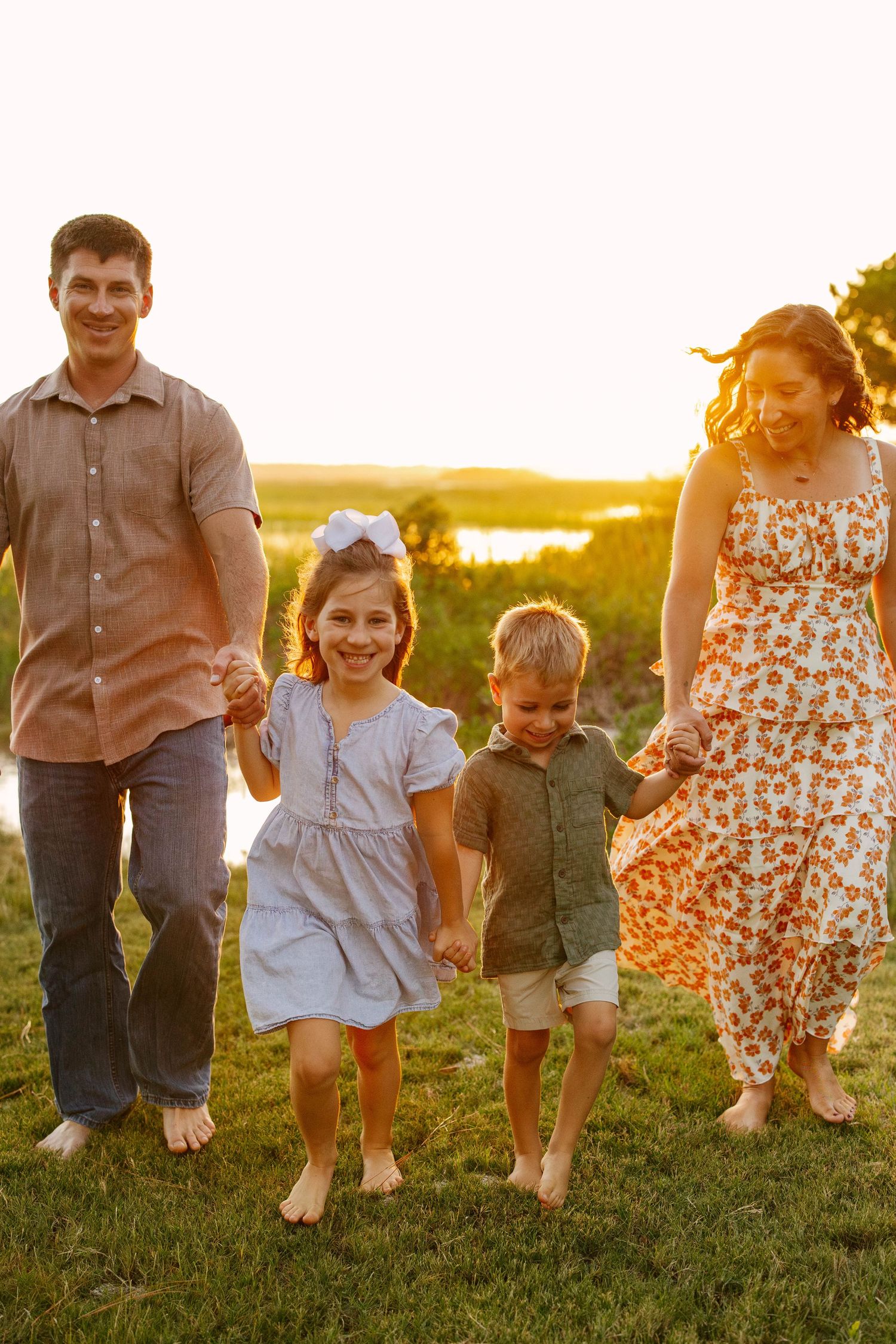 A family sits together on a waterfront boardwalk at sunset with string lights in background.