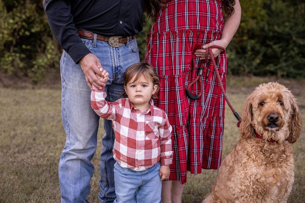 A child poses with the family dog and his parent's legs in the background.