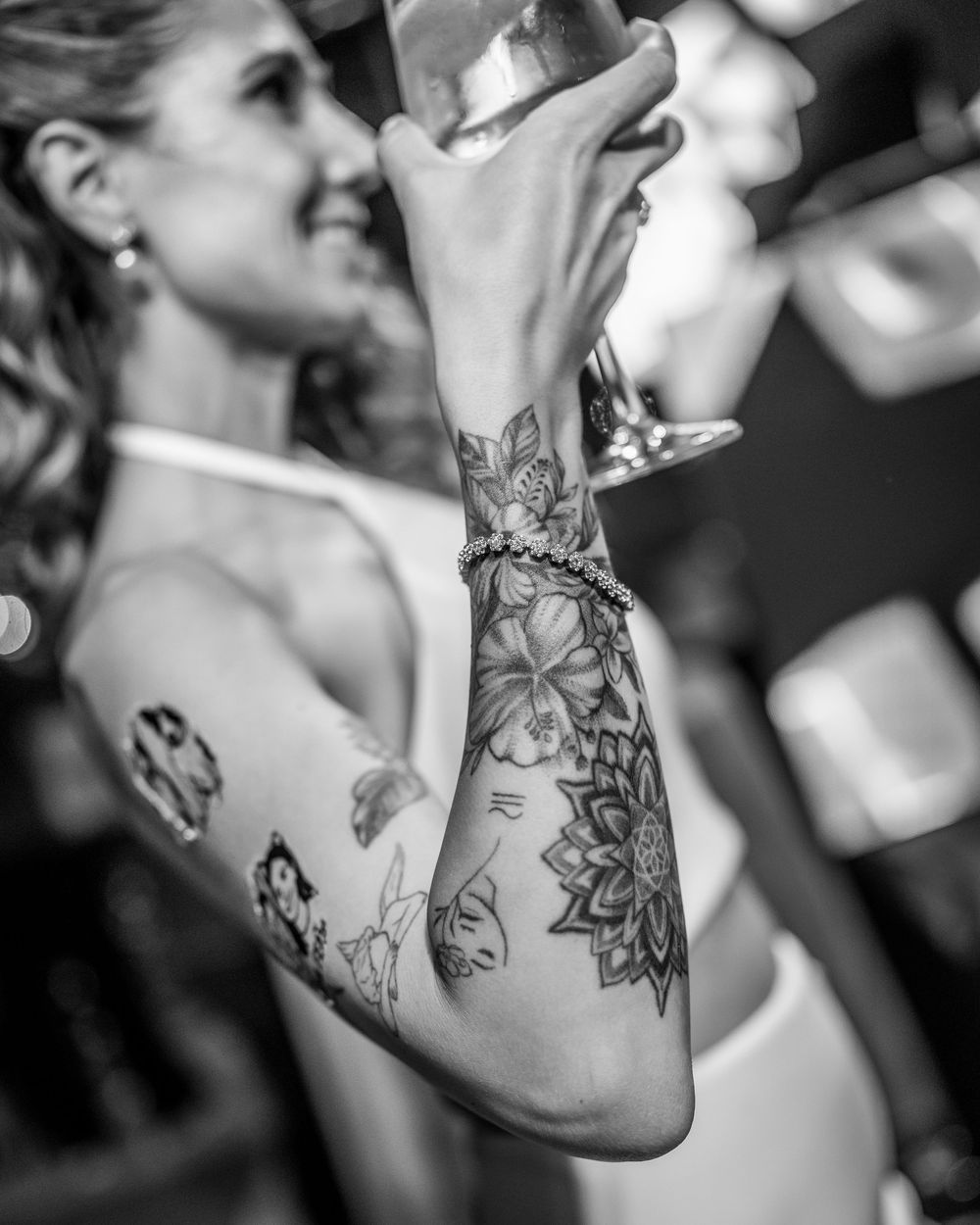 Close-up of bride's arm featuring intricate floral and mandala tattoos at wedding reception.