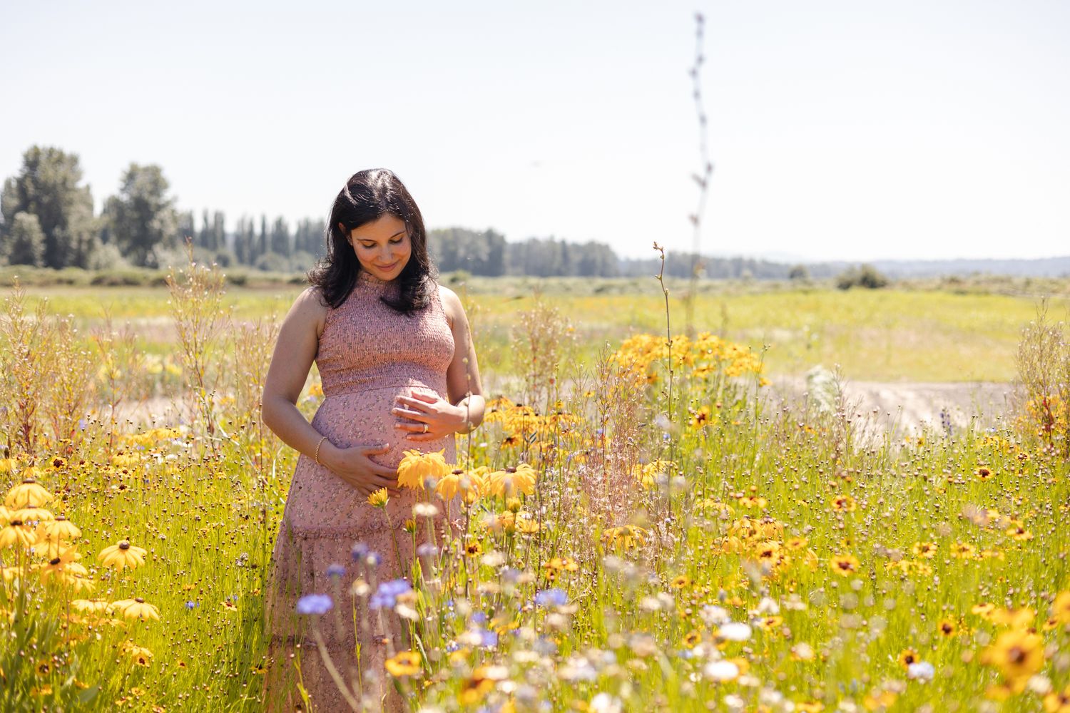 Woman in pink dress stands among wildflowers in sunny meadow.