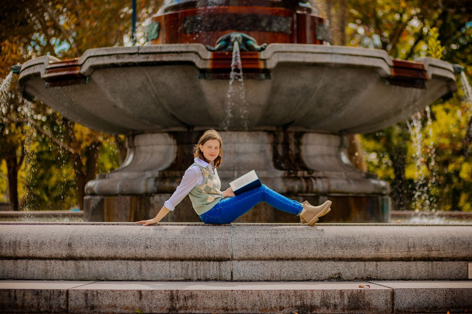 young woman sits on a fountain reading a book