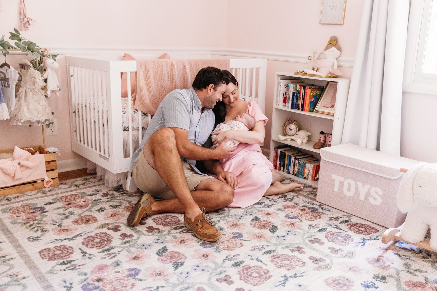 Tender family moments captured in a soft pink nursery with toys and baby furniture.