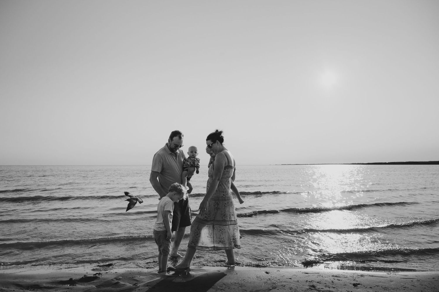 Family shares an intimate moment together on a serene beach during sunset.