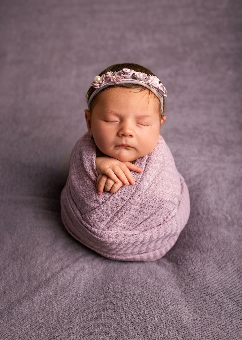 Sleeping newborn wrapped in soft pink knitted blanket on grey backdrop during professional photo session.