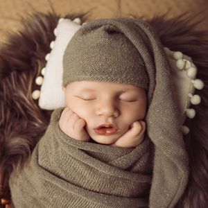 Newborn baby swaddled in soft gray knit wrap with matching hat against dark background.