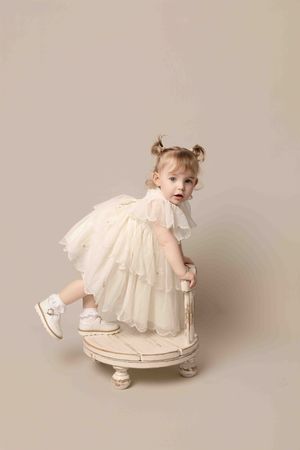 A series of four photos showing a baby in a white vintage dress crawling and playing on a light beige backdrop.